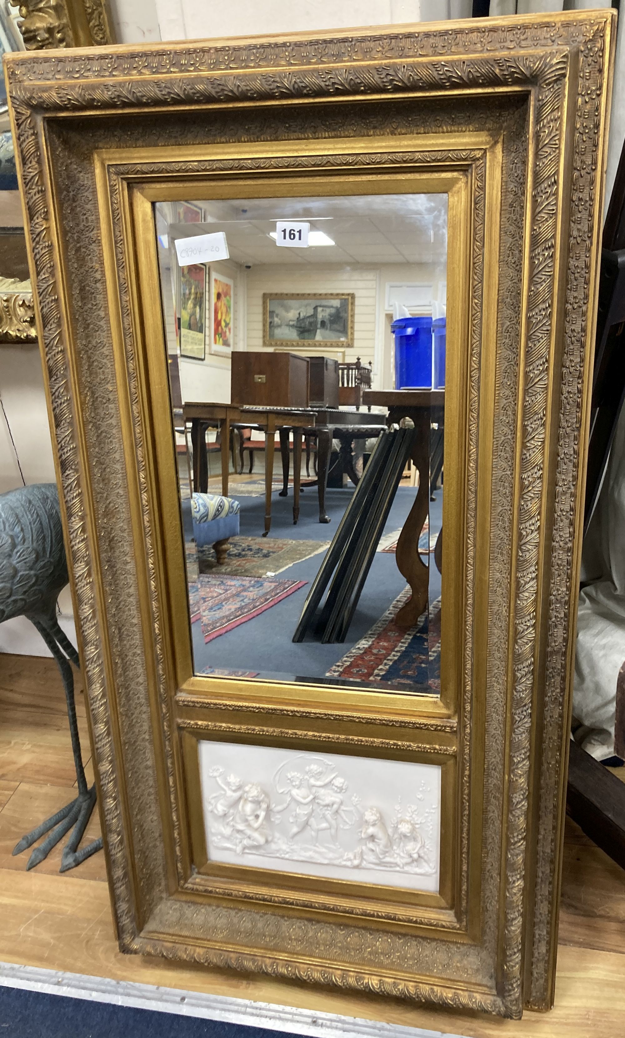 A gilt framed mirror, the base inset with a composition relief depicting putti at play, width 56cm, height 105cm